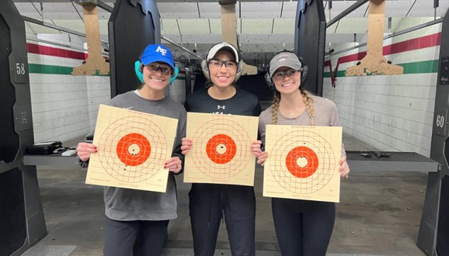 Shooters holding target sheets after accuracy drill at indoor shooting range